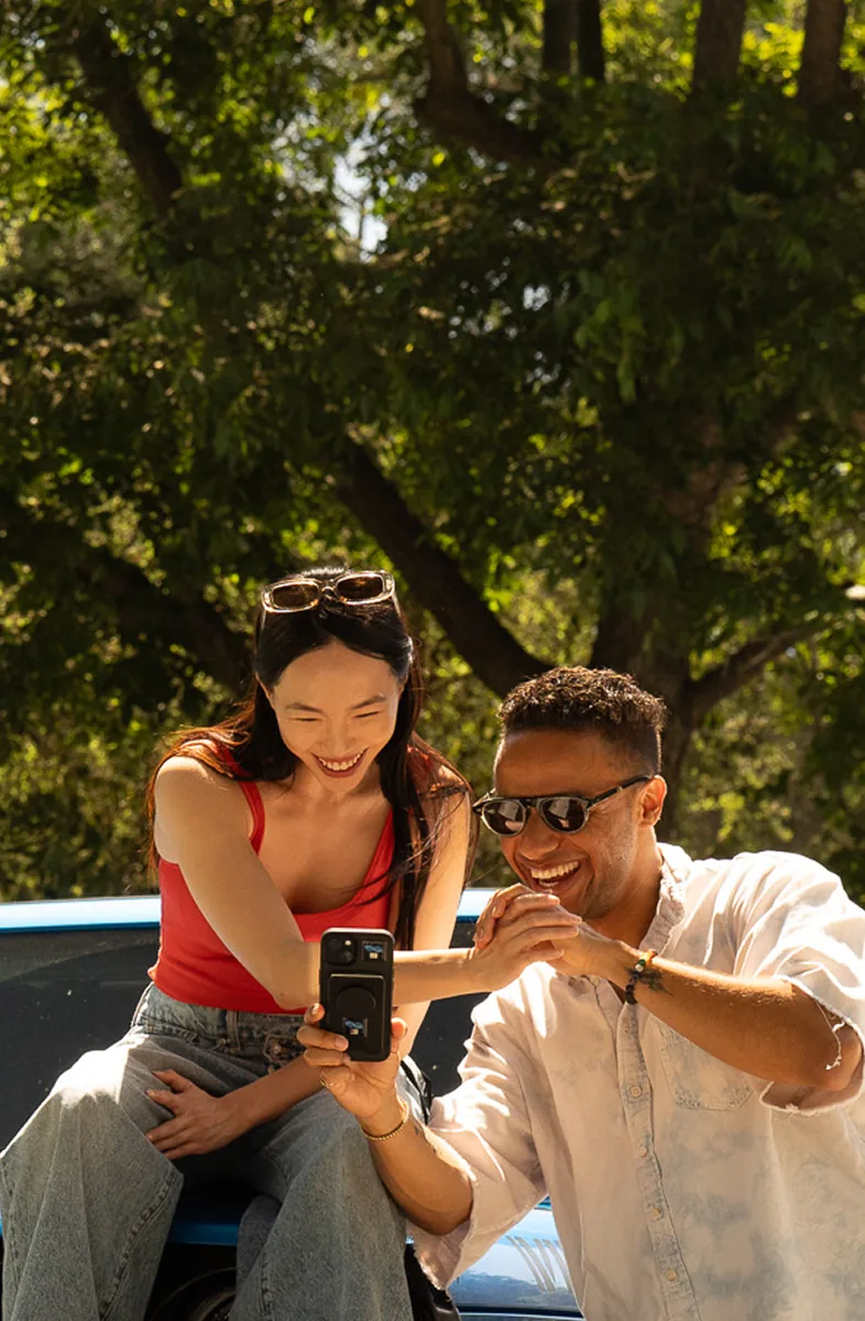 Two friends checking a Bidbus offer on a phone next to their car